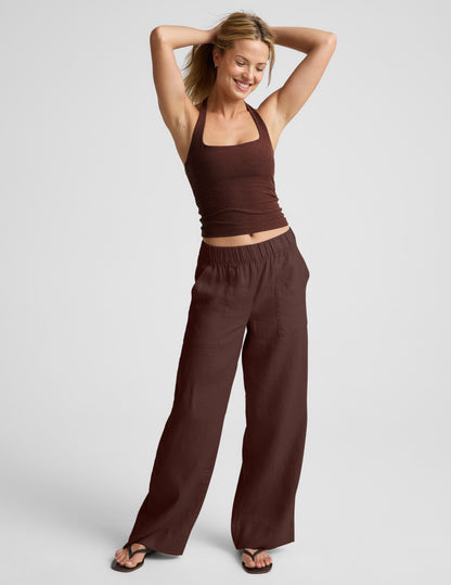 Woman wearing a brown halter tank top and brown linen pants against a plain background.
