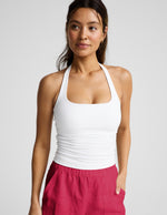 Woman wearing a white halter tank top and red linen shorts against a plain background.