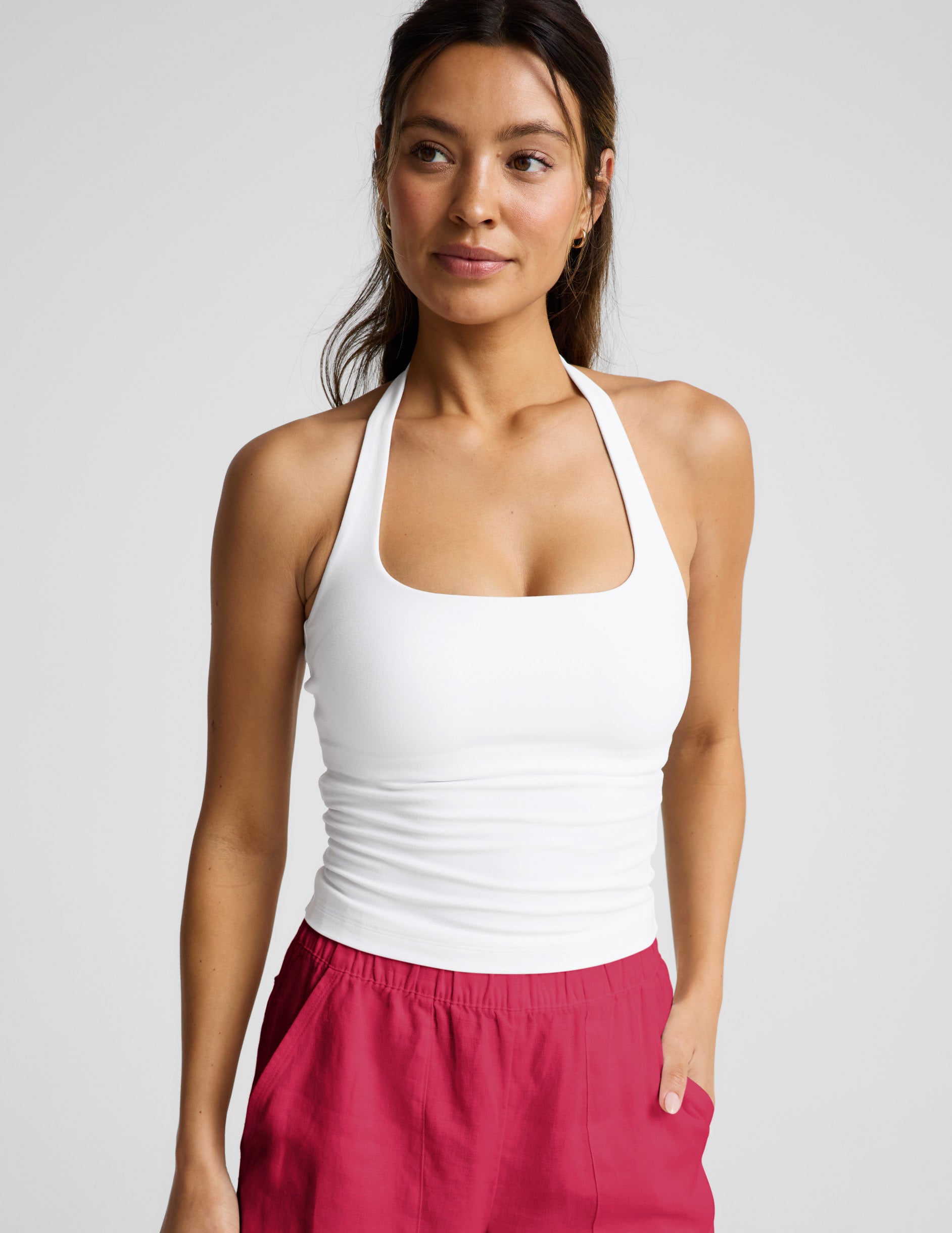 Woman wearing a white halter tank top and red linen shorts against a plain background.