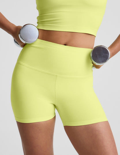 Woman wearing Yellow Spacedye™ Keep Pace 3" Short paired with a matching tank top while holding dumbbells.