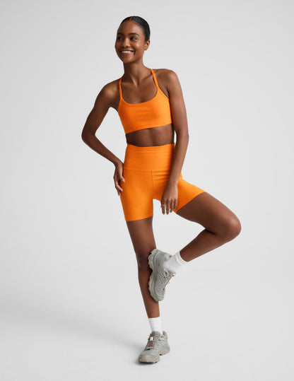 Woman wearing Orange Spacedye™ Keep Pace 5" Biker Short paired with a matching sports bra and grey sneakers.