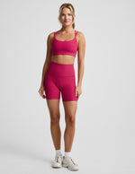 Woman wearing Fuchsia Spacedye™ Keep Pace 5" Biker Short paired with a matching sports bra and sneakers.
