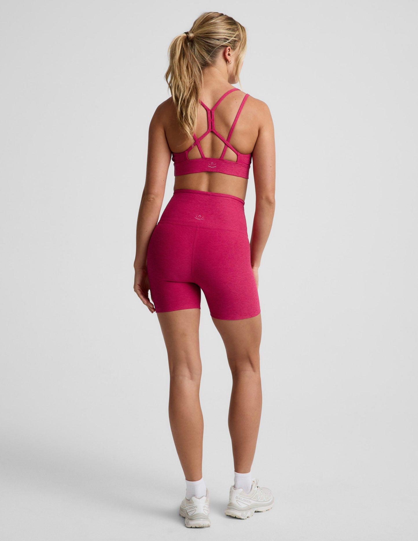 Rear view of woman wearing Fuchsia Spacedye™ Keep Pace 5" Biker Short with a matching sports bra and white sneakers.