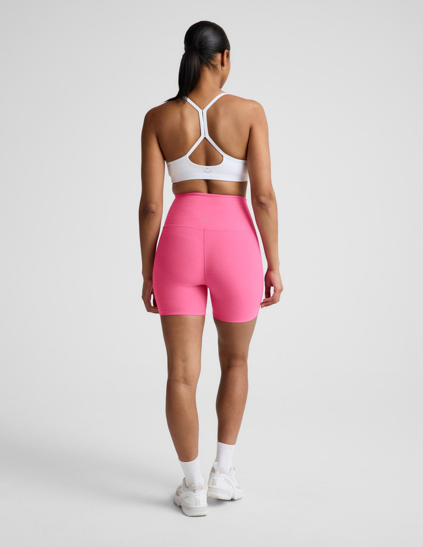 Woman wearing Pink Spacedye Keep Pace 5" Biker Short™ with a white sports bra and sneakers, rear view.