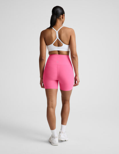 Woman wearing Pink Spacedye Keep Pace 5" Biker Short™ with a white sports bra and sneakers, rear view.