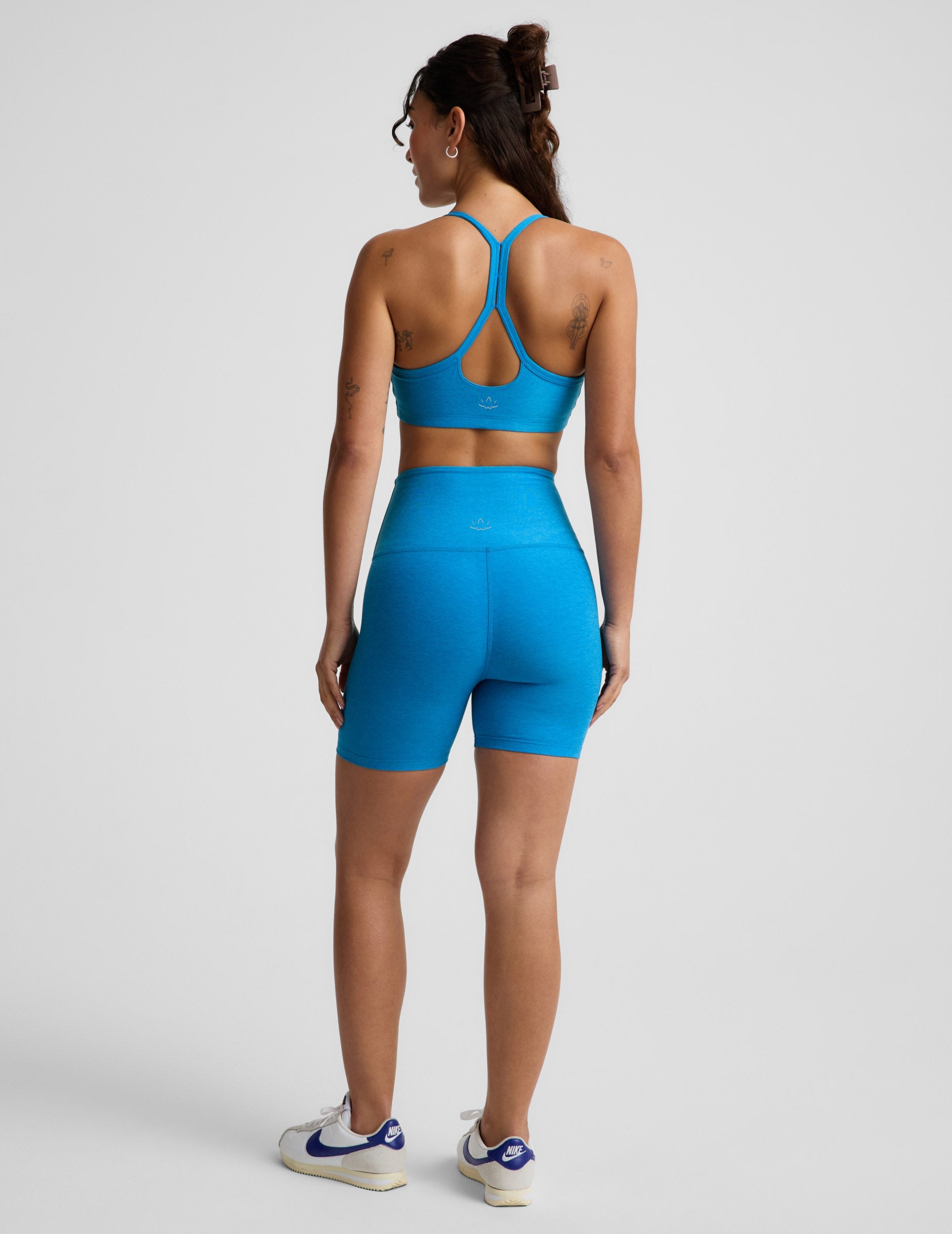 Woman wearing Blue Spacedye™ Keep Pace 5" Biker Short from a rear view, paired with a matching sports bra and sneakers.