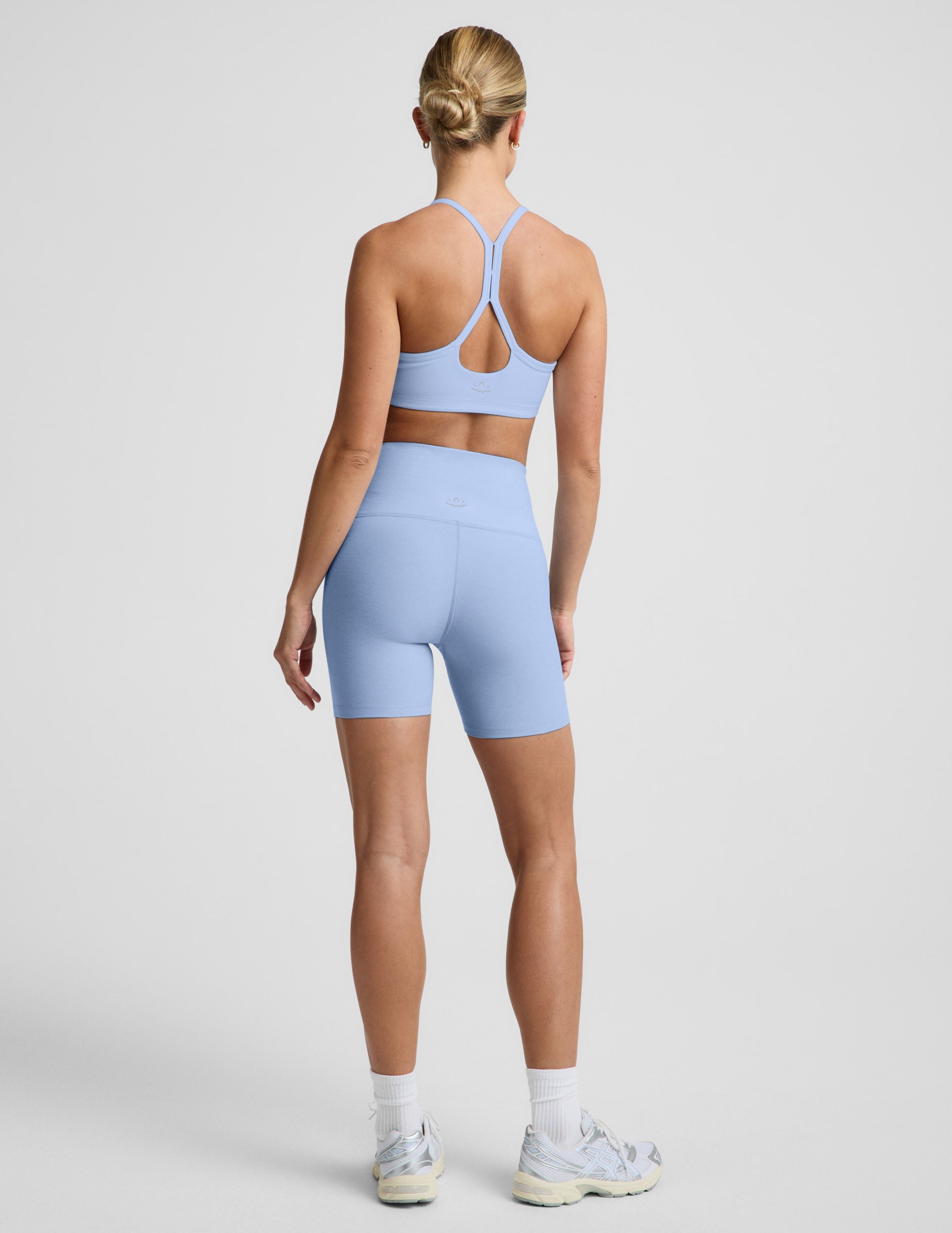 Woman wearing Blue Spacedye™ Keep Pace 5" Biker Short, rear view, paired with a matching sports bra and sneakers.