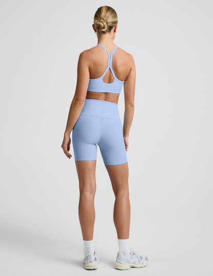 Woman wearing Blue Spacedye™ Keep Pace 5" Biker Short, rear view, paired with a matching sports bra and sneakers.