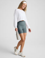 Woman wearing Green Spacedye Keep Pace 5" Pocket Short™ paired with a white long-sleeve crop top and sneakers.