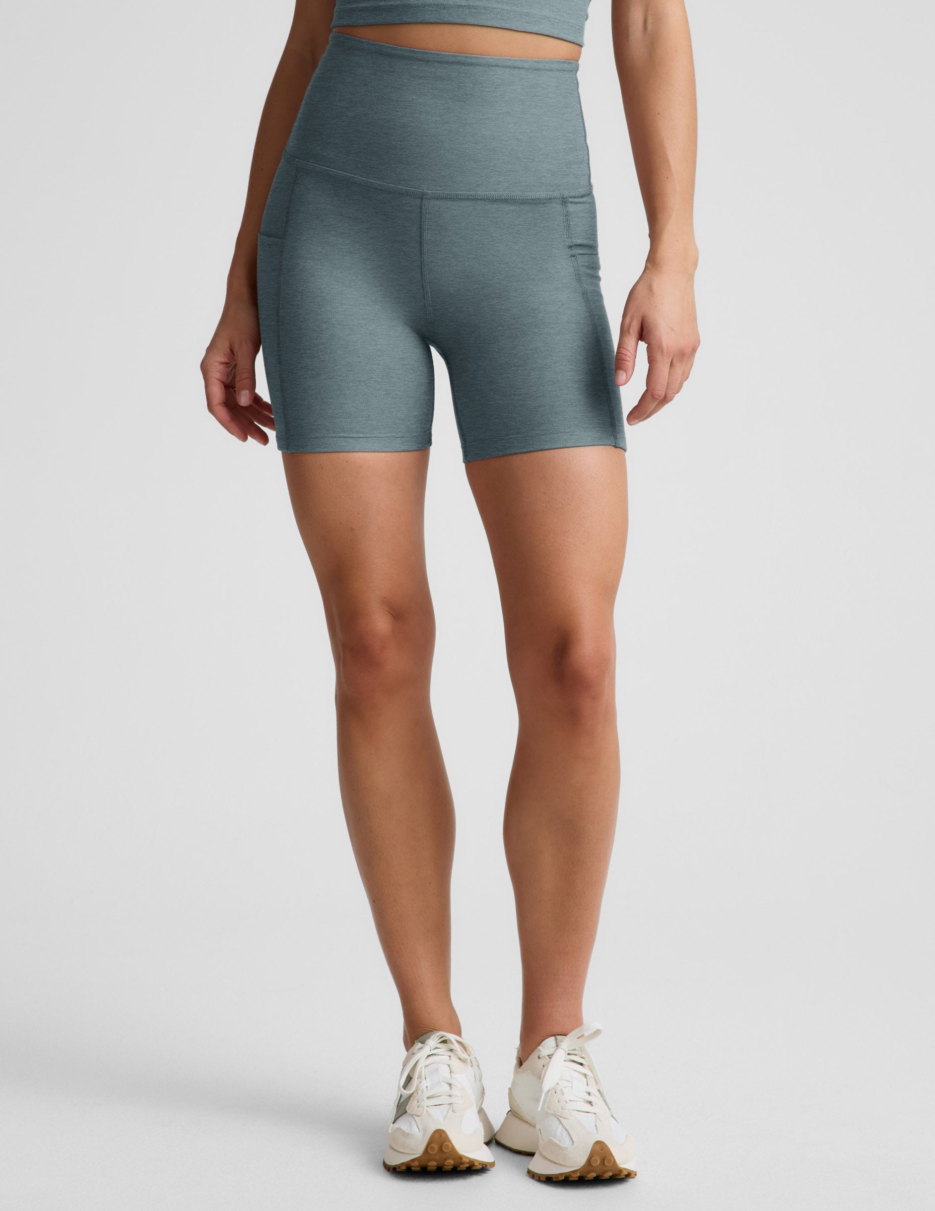 Woman wearing green Spacedye Keep Pace 5" Pocket Short™ with a matching top and cream sneakers, featuring side pockets.
