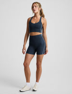 Woman wearing Navy Spacedye™ Streamline 5" Short with white piping, a matching racerback tank, and white sneakers.