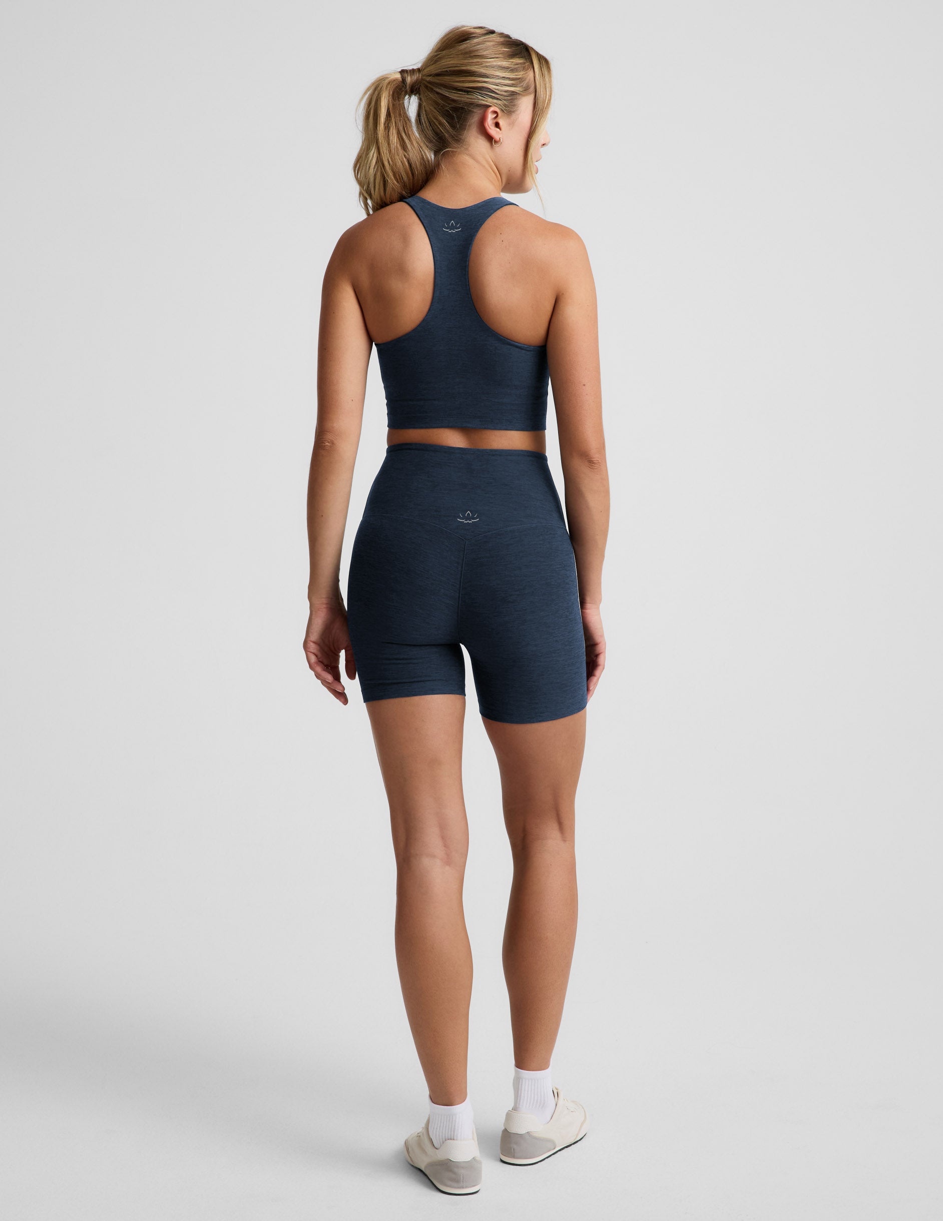 Woman wearing Navy Spacedye™ Streamline 5" Short, Rear view, paired with a matching navy racerback tank and white sneakers.