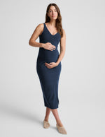 Woman wearing a navy blue sleeveless maternity dress against a light gray background.