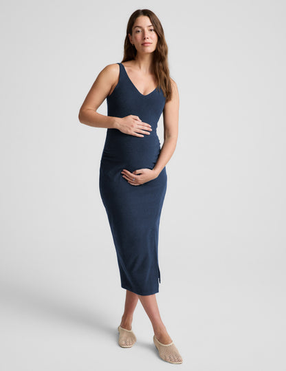 Woman wearing a navy blue sleeveless maternity dress against a light gray background.