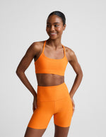 Woman wearing an orange sports bra and biker shorts against a plain background.