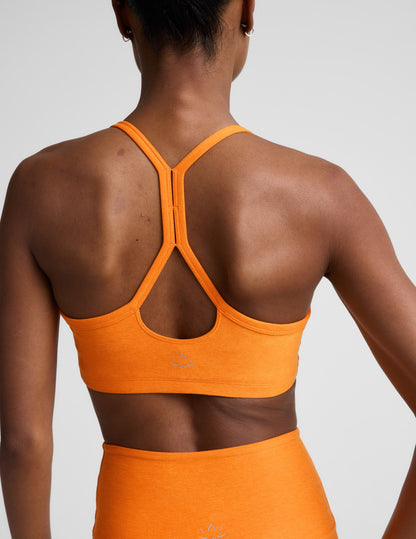 Woman wearing an orange sports bra and biker shorts against a plain background.
