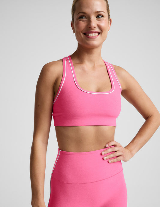 Woman wearing a pink sports bra with white trim and pink leggings against a plain background.
