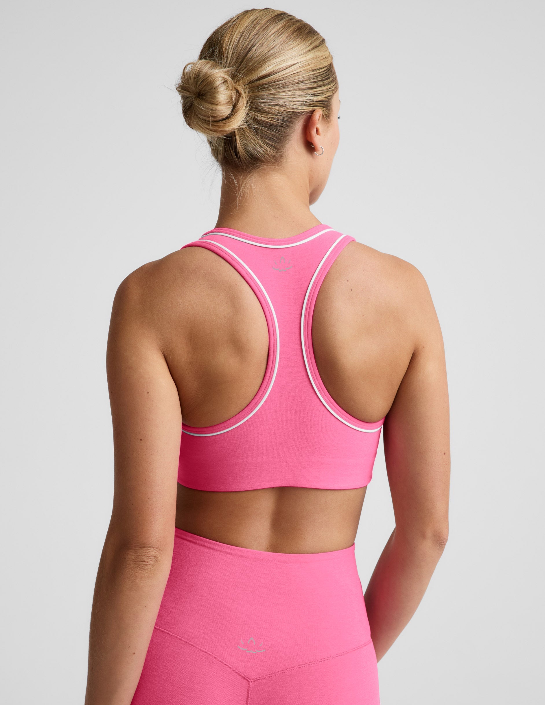 Woman wearing a pink sports bra with white trim and pink leggings against a plain background.