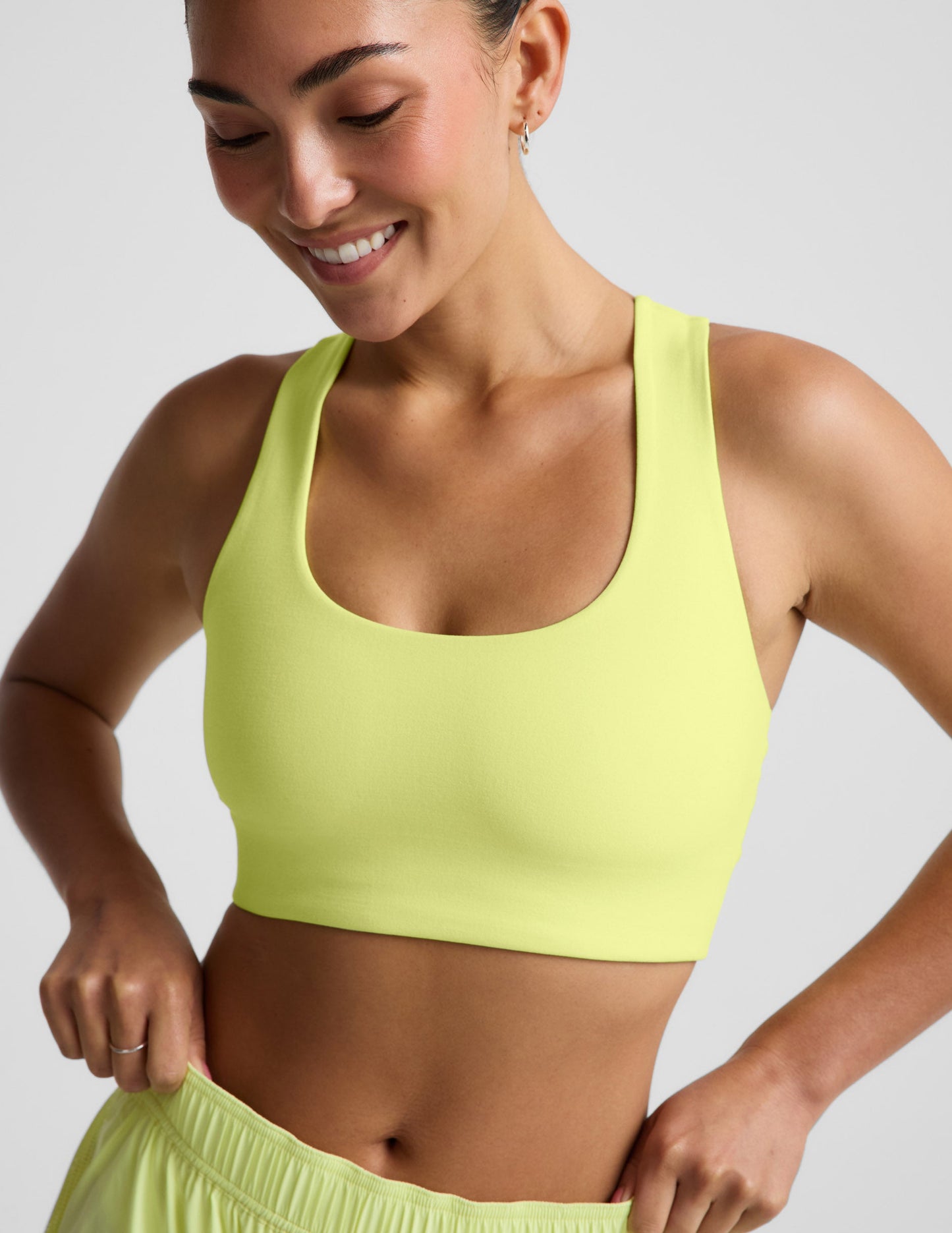 Woman wearing a bright yellow sports bra and shorts against a light gray background.