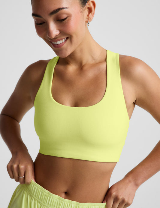 Woman wearing a bright yellow sports bra and shorts against a light gray background.