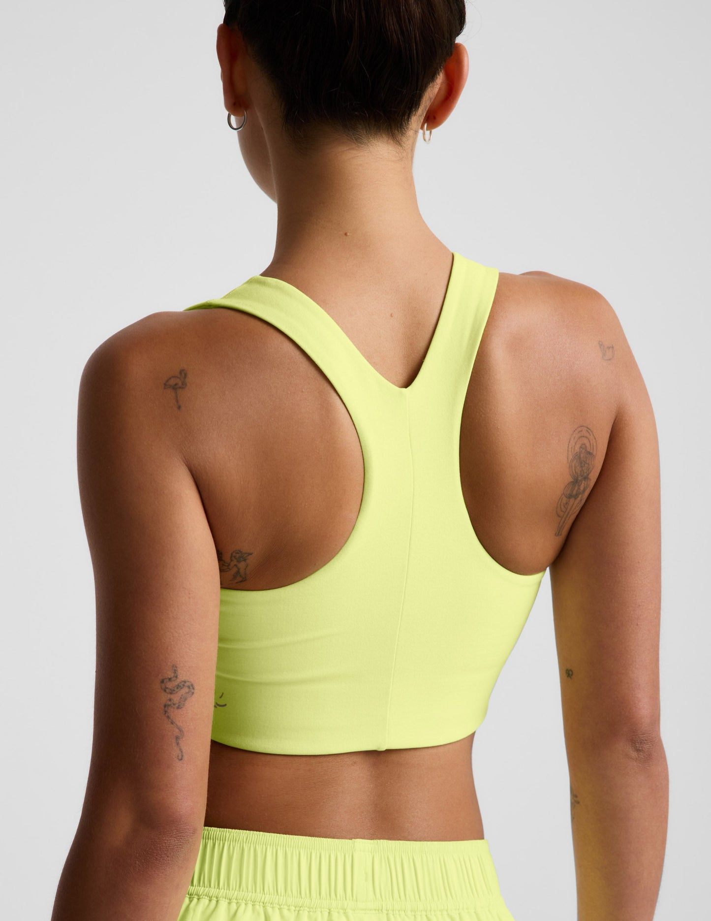 Woman wearing a bright yellow sports bra and shorts against a light gray background.