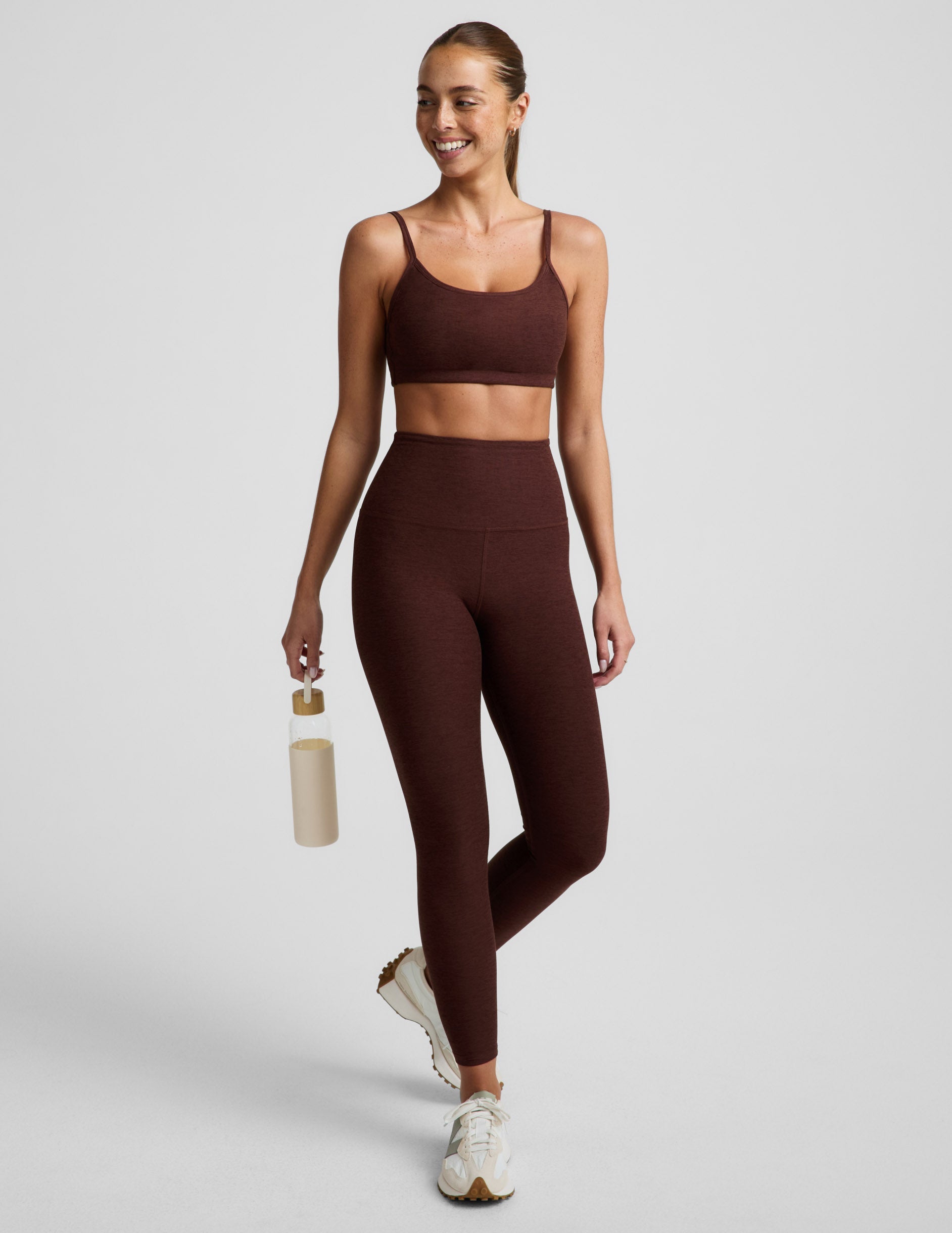 Woman wearing a brown sports bra and brown leggings against a plain background.
