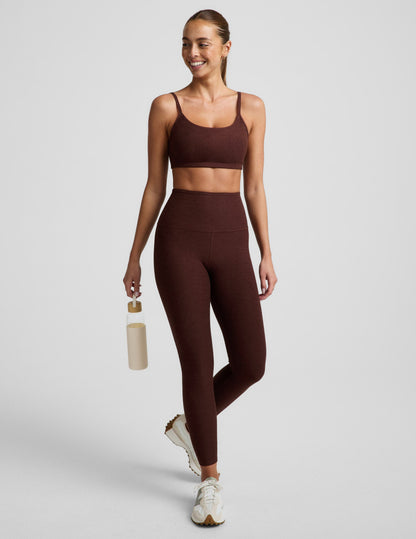 Woman wearing a brown sports bra and brown leggings against a plain background.