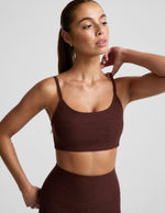 Woman wearing a brown sports bra and brown leggings against a plain background.