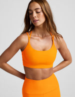 Woman wearing an orange strappy bra and orange leggings against a plain background.