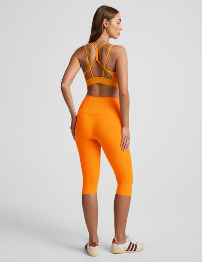 Woman wearing an orange strappy bra and orange leggings against a plain background.