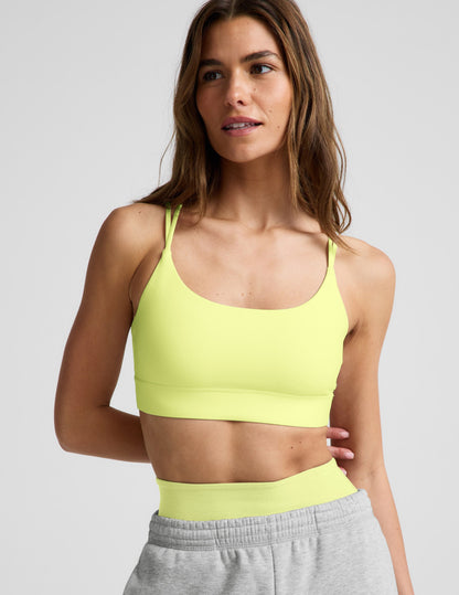 Woman wearing a lime sports bra and gray sweatpants against a plain background.