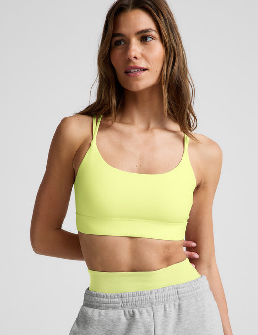 Woman wearing a lime sports bra and gray sweatpants against a plain background.