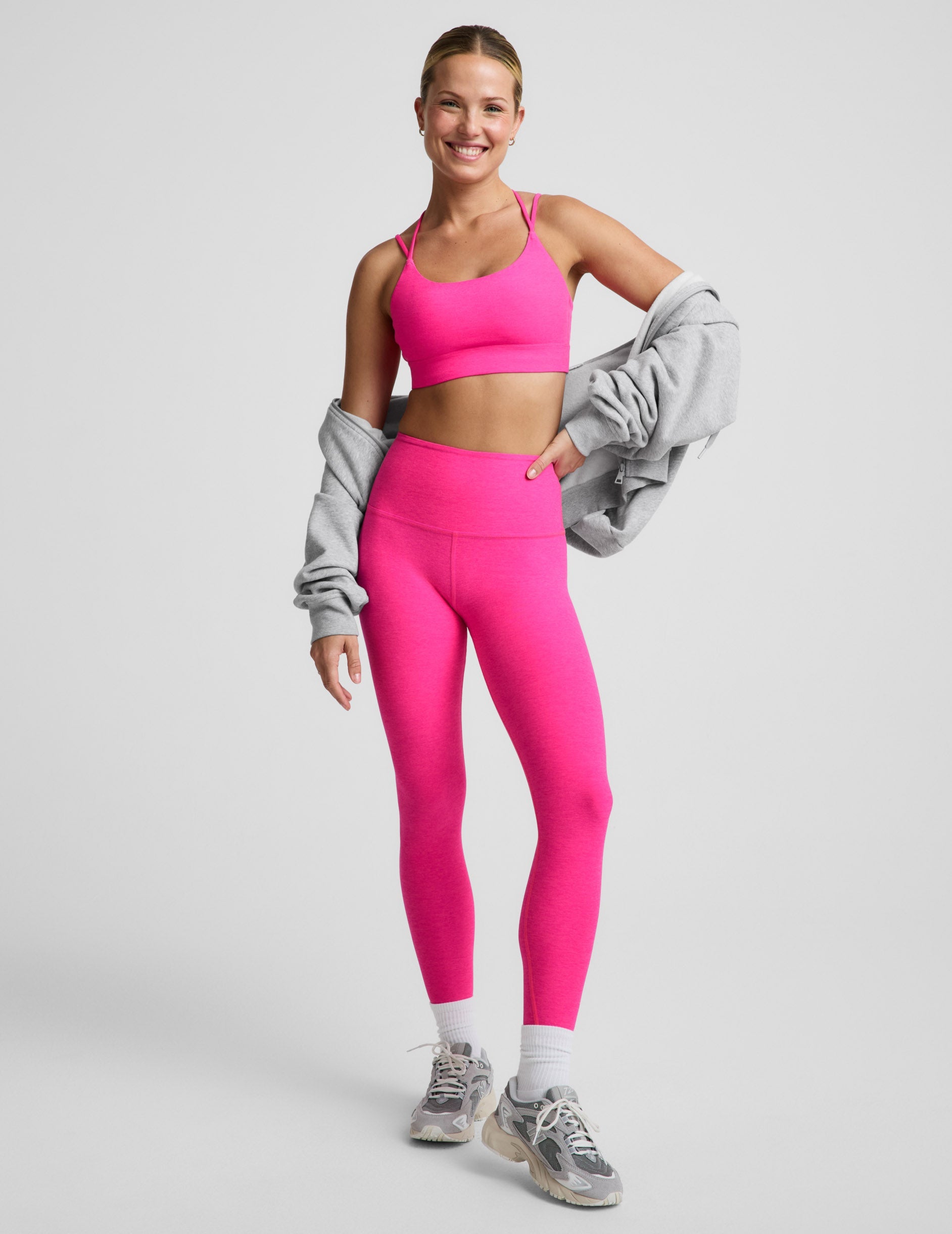 Woman wearing a bright pink strappy sports bra and pink leggings against a plain background.