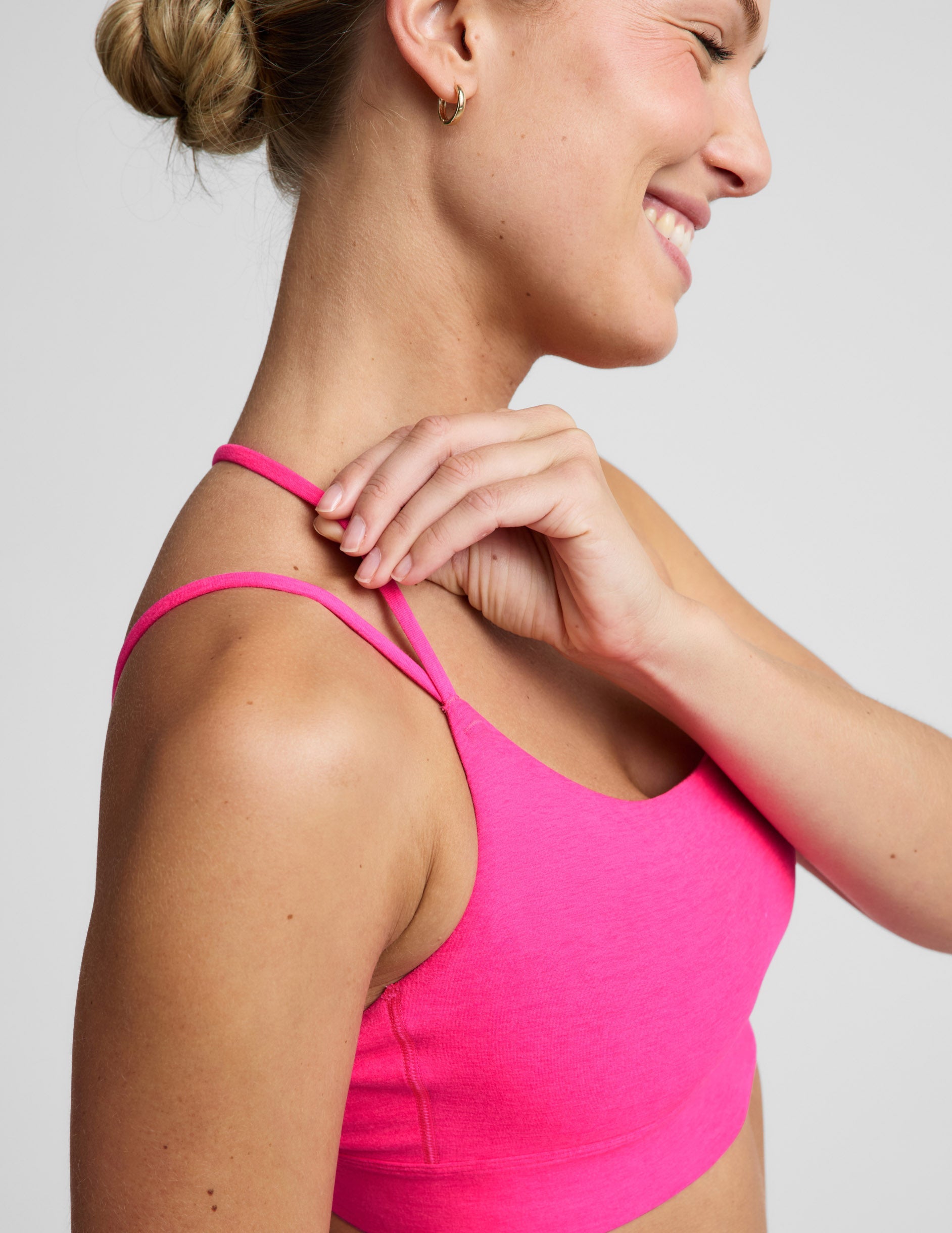 Woman wearing a bright pink strappy sports bra and pink leggings against a plain background.