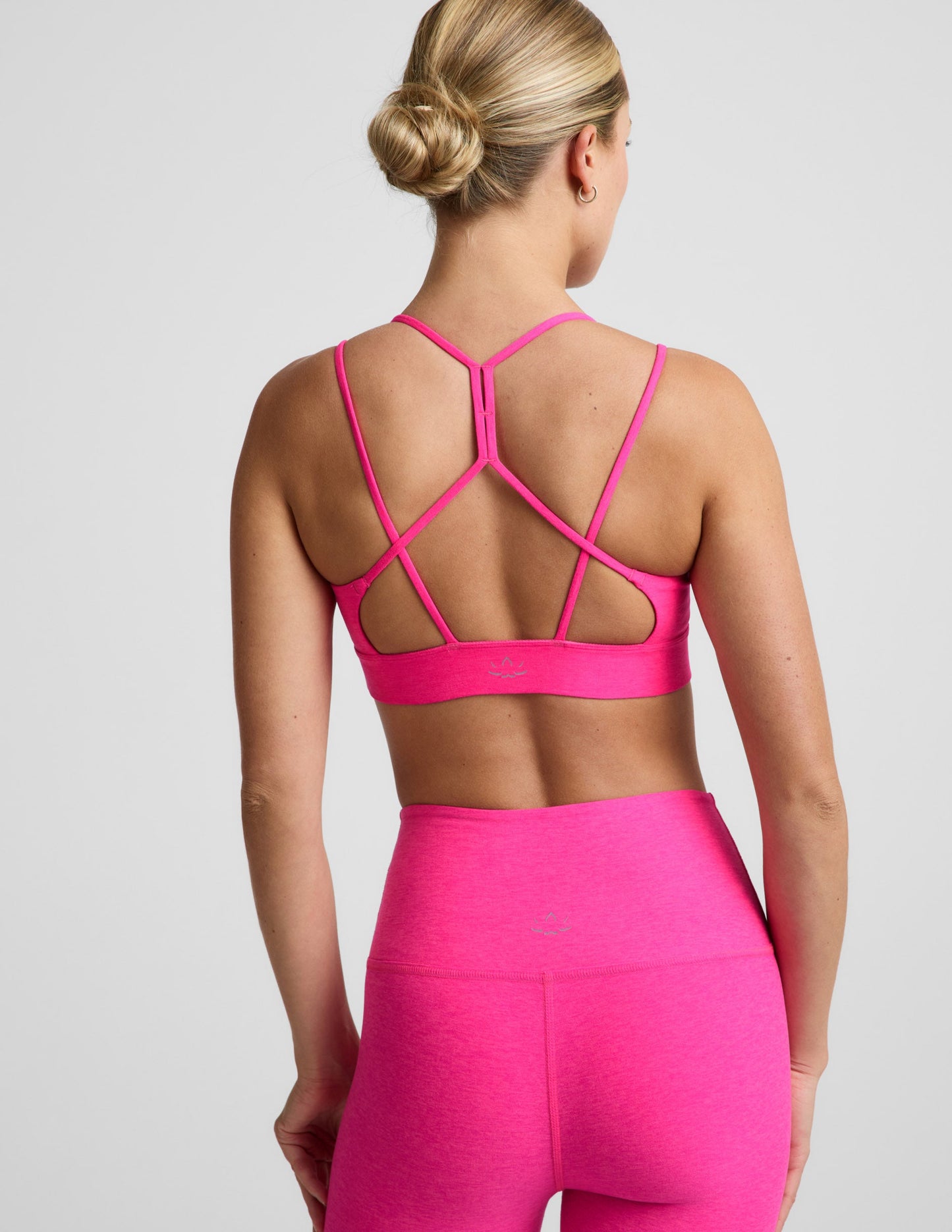 Woman wearing a bright pink strappy sports bra and pink leggings against a plain background.