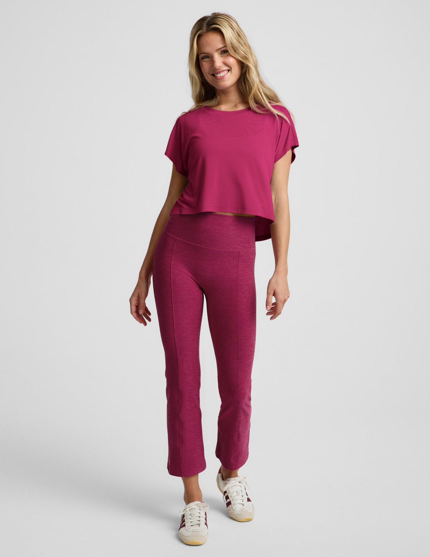 Woman wearing a magenta cropped short sleeve and magenta pintuck capri pants against a plain background.