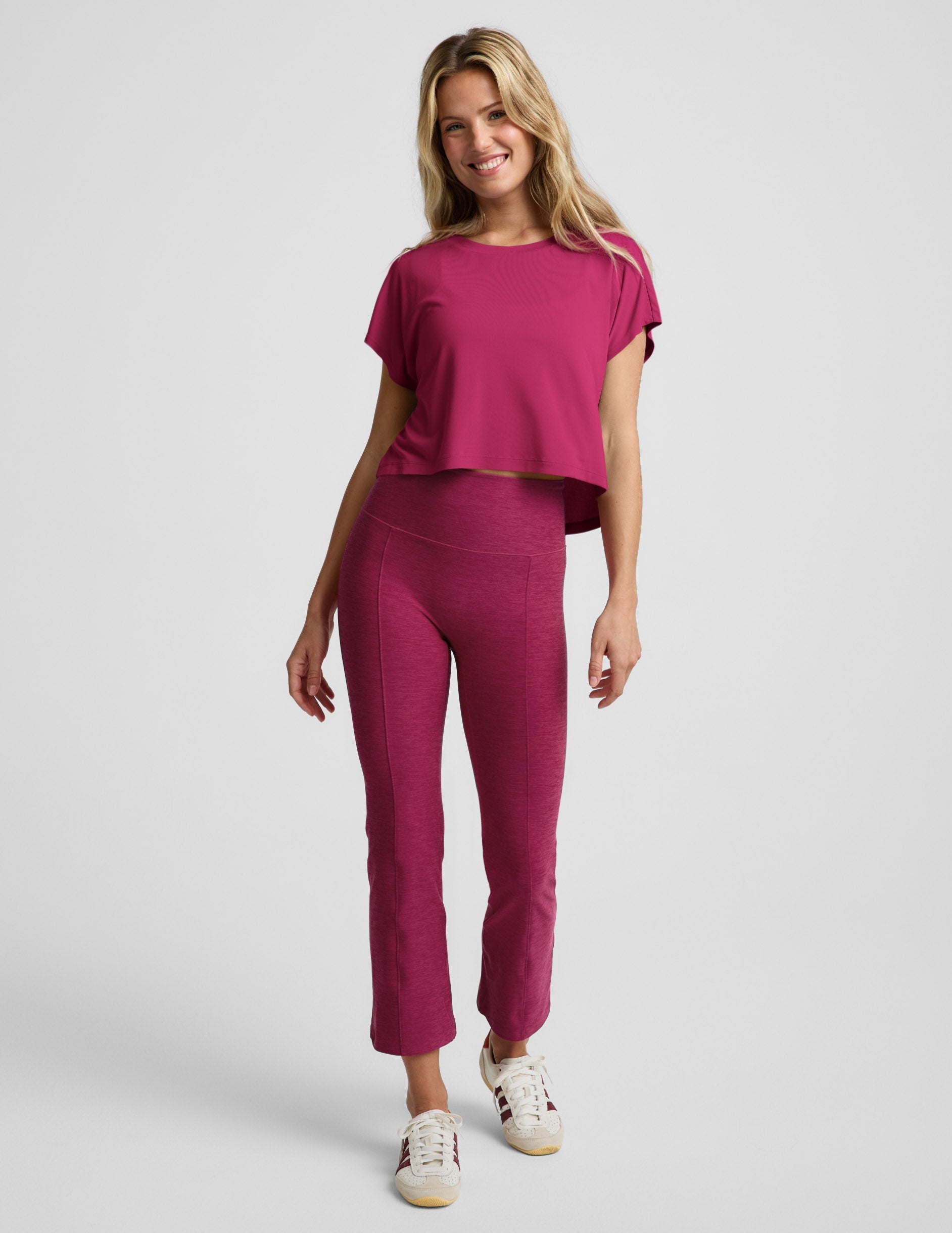 Woman wearing a magenta cropped short sleeve and magenta pintuck capri pants against a plain background.