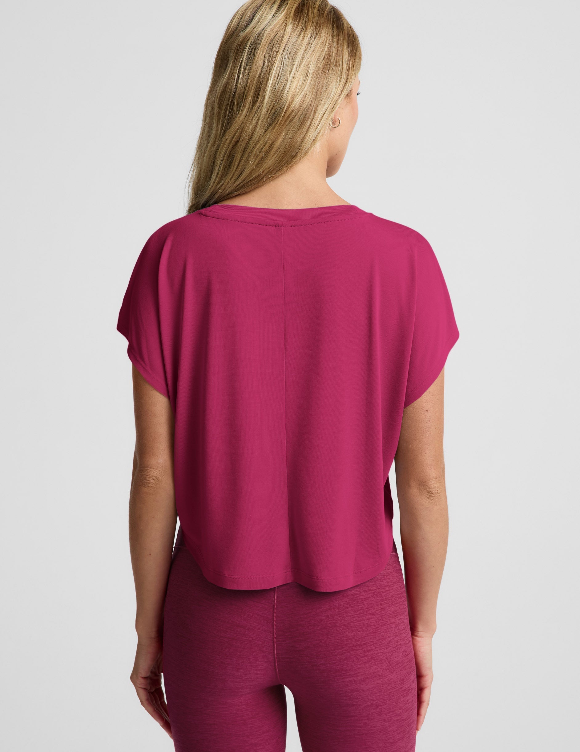 Woman wearing a magenta cropped short sleeve and magenta pintuck capri pants against a plain background.