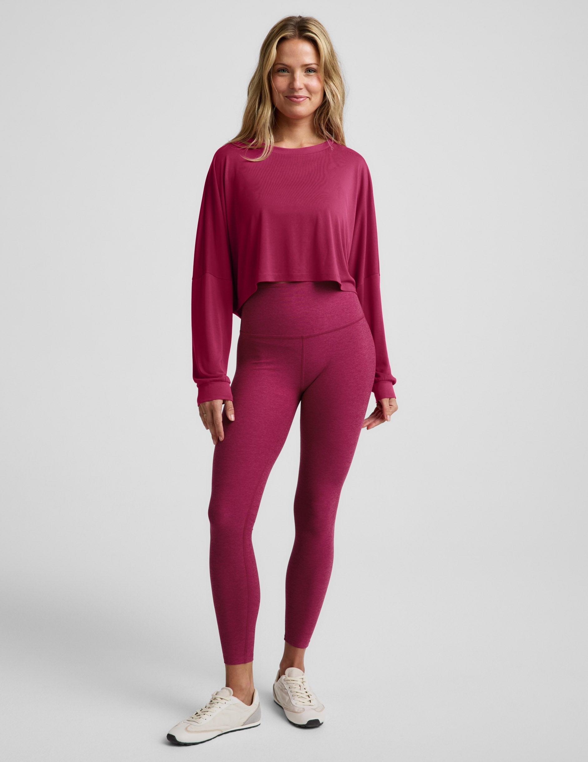 Woman wearing a cropped magenta long sleeve top and high-waisted midi length leggings against a plain background.