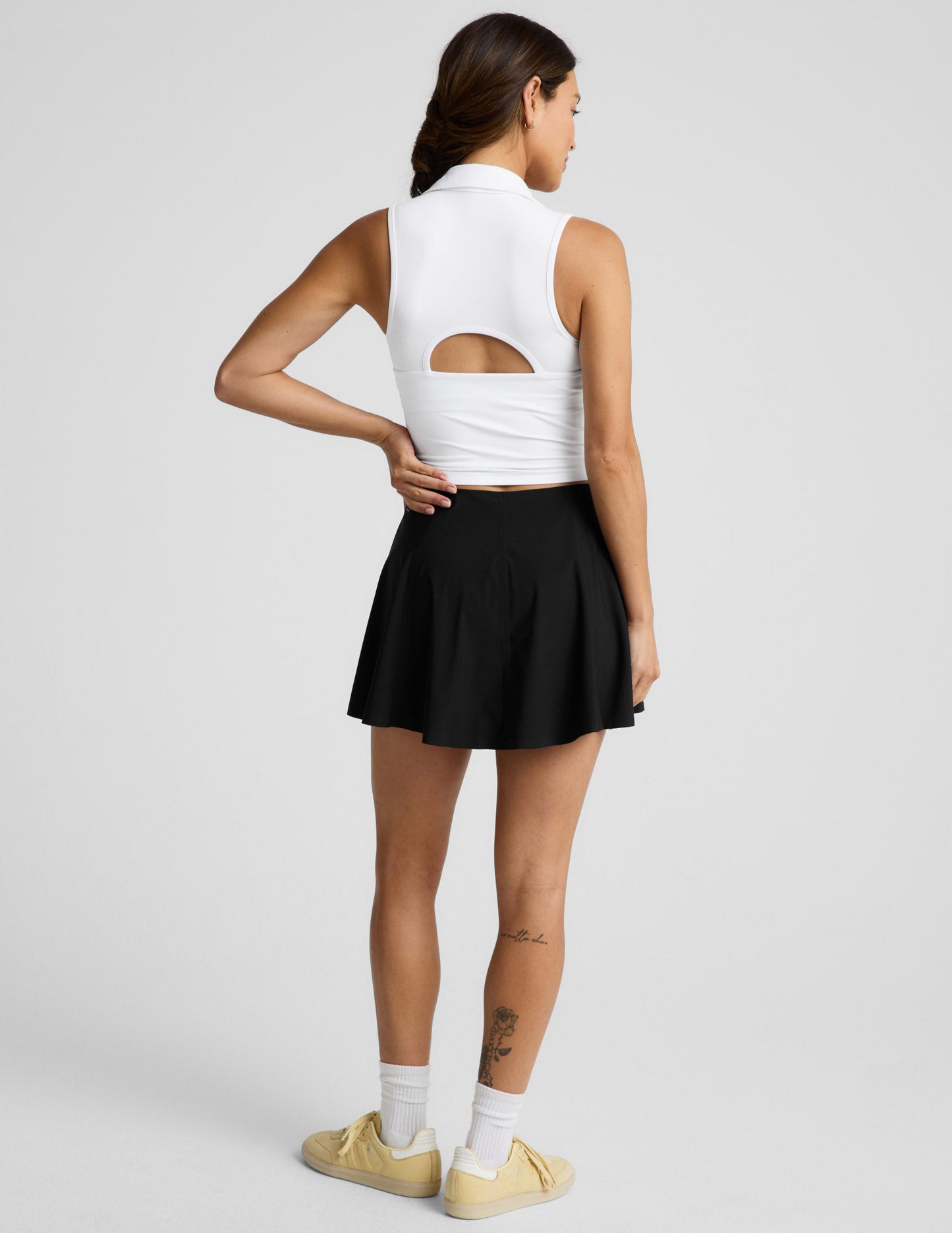Woman wearing the Black You're A force Skirt™ with a white sleeveless top and yellow sneakers, shown from a rear view.