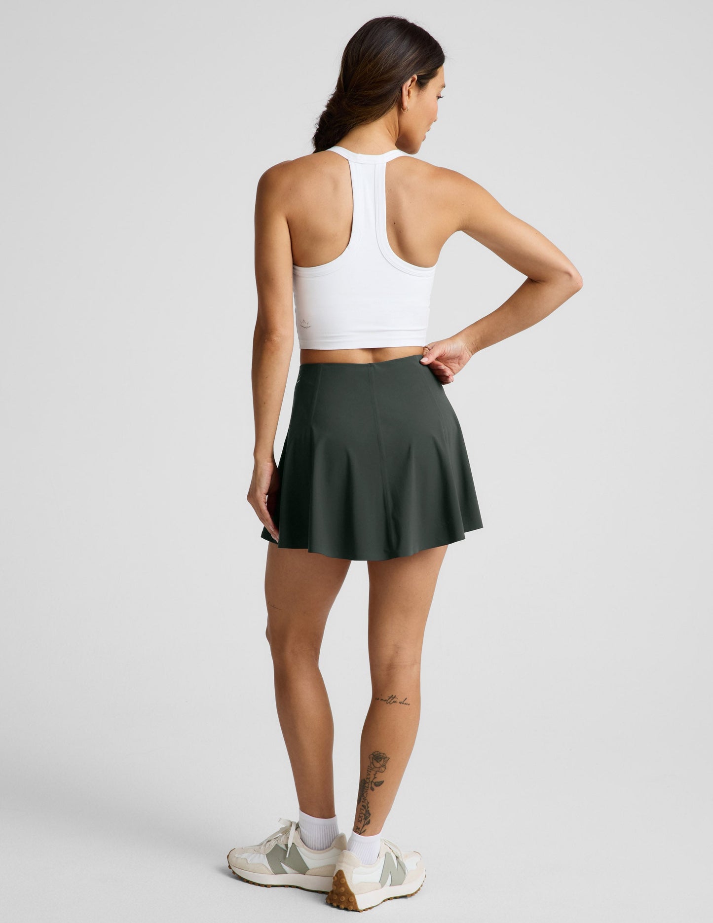 Woman wearing Green You're A Force Skirt™ from a rear view, paired with a white racerback sports bra and sneakers.