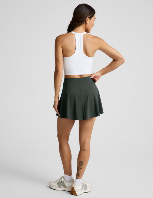 Woman wearing Green You're A Force Skirt™ from a rear view, paired with a white racerback sports bra and sneakers.