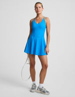 Woman wearing a blue tennis dress holding a racket on a light gray background.