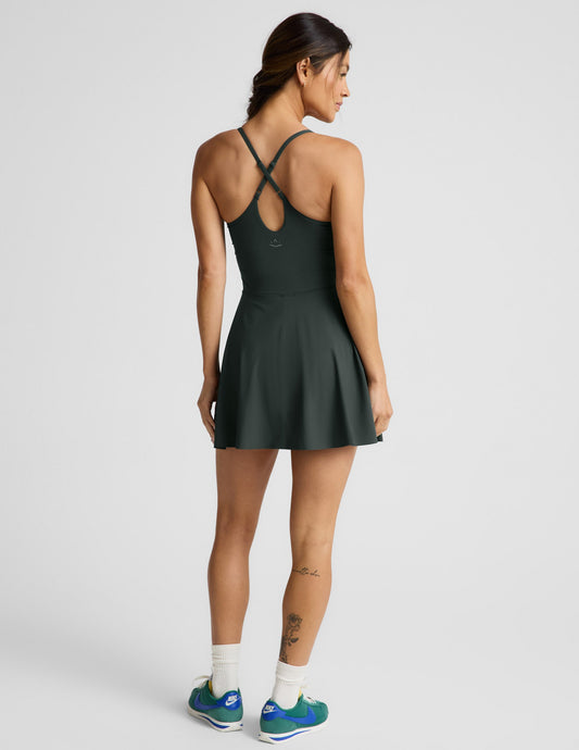 Woman wearing a dark green athletic dress with built-in shorts against a plain background.