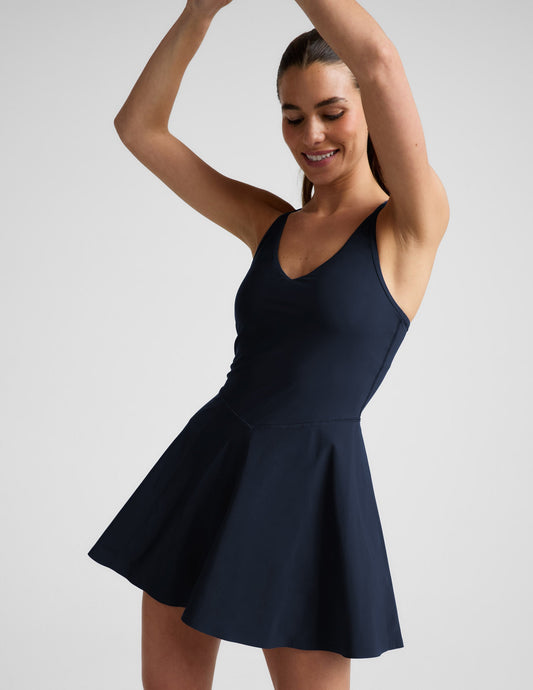 Woman wearing a navy blue athletic dress with built-in shorts against a plain background.