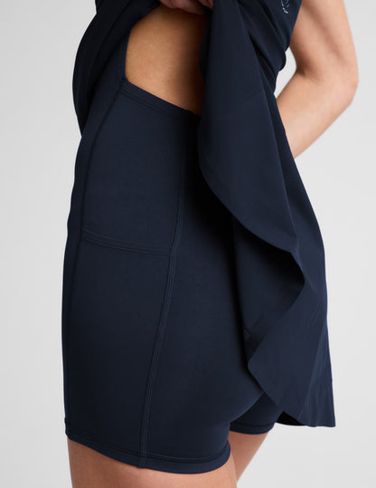 Woman wearing a navy blue athletic dress with built-in shorts against a plain background.
