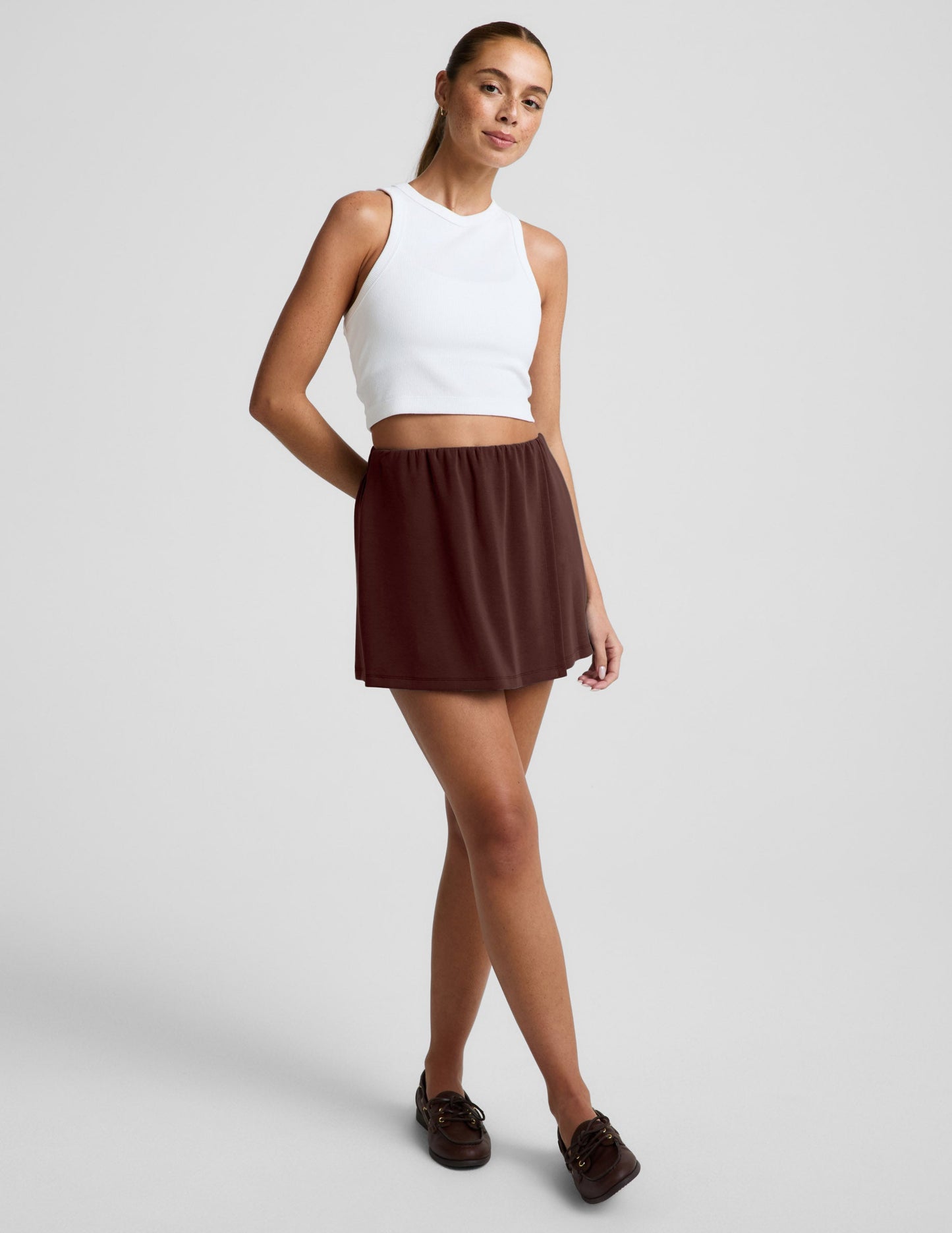 Woman wearing brown Luxe Sandwash Skort™ with a white cropped tank top and dark brown leather boat shoes.