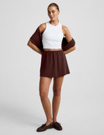 Woman wearing brown Luxe Sandwash™ Skort with a white ribbed tank top and a brown sweater draped over her shoulders.