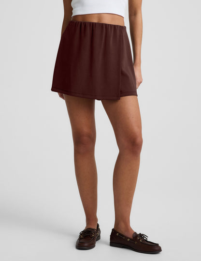 Woman wearing Brown Luxe Sandwash Skort™ paired with a white tank top and brown loafers.