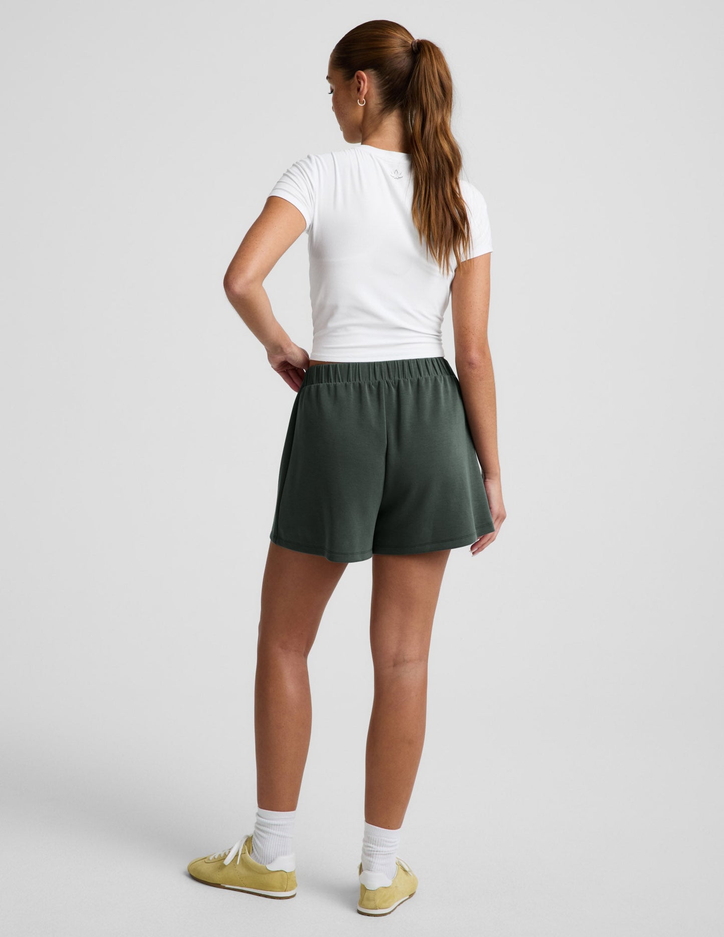 Rear view of woman wearing green Luxe Sandwash Skort™ with a white short-sleeve t-shirt and yellow sneakers.